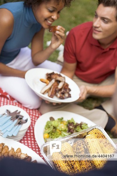 Couple with grilled spare ribs  corn on the cob  salad  on grass