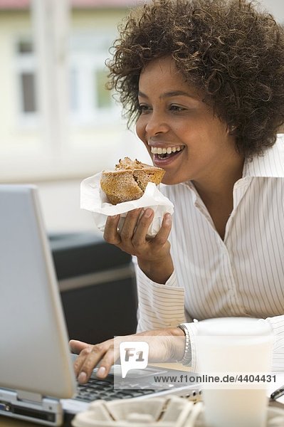 Frau isst Muffin während der Arbeit am computer