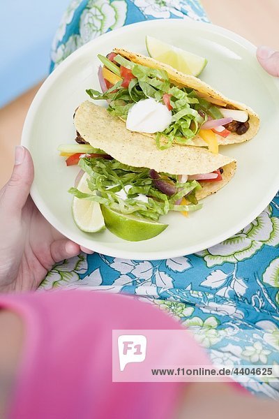 Frau hält Platte mit zwei tacos