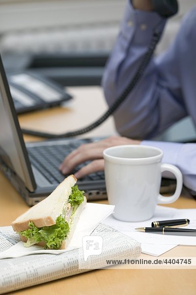 Kaufmann auf Telefon  Sandwich und Kaffee auf Schreibtisch