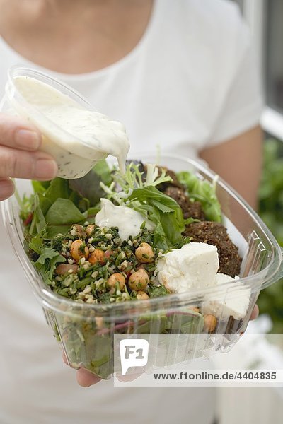 Frau Gießen Dressing über Salat in Kunststoff-container