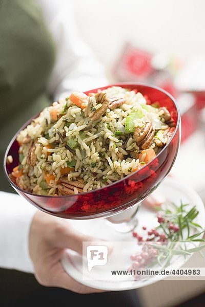 Woman holding bowl of vegetable rice with pecans (Christmas)