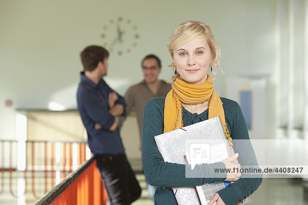 Young woman holding book with students standing in background