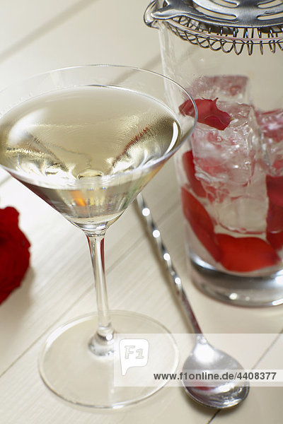 Martini-Glas mit Martini und Shaker mit Eiswürfeln und Rosenblättern  Nahaufnahme.
