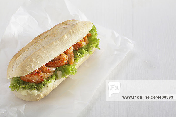 Baguette roll filled with crayfish against white background.