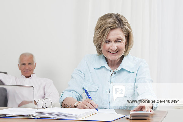 Woman doing paperwork with man sitting in background