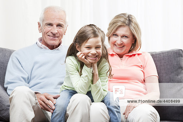 Enkelin (6-7) sitzend auf dem Schoß der Großeltern mit Kopf in der Hand  lächelnd  Porträt