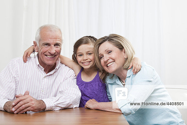 Enkelin (6-7) Arm um Großeltern  lächelnd  Portrait