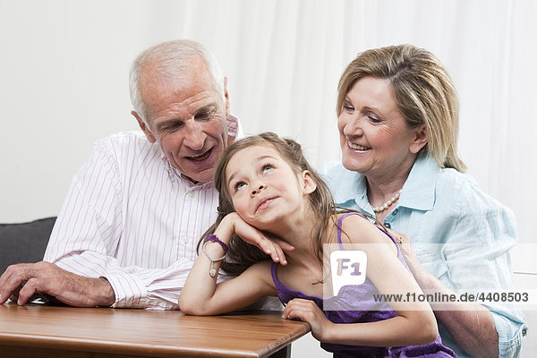 Enkelin (6-7) Kopf in Hand mit den Großeltern  lächelnd