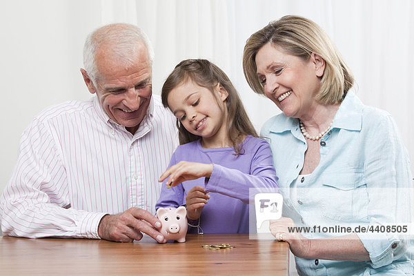 Enkelin (6-7) und Großeltern mit Sparschwein  lächelnd