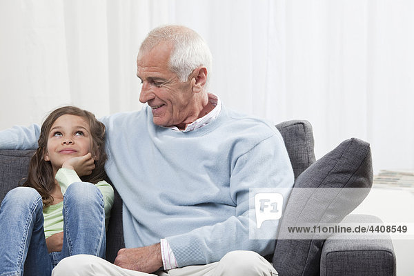 Enkelin (6-7) und Großvater auf der Couch sitzend  lächelnd