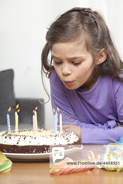 Mädchen (6-7) beim Ausblasen von Kerzen auf Geburtstagskuchen