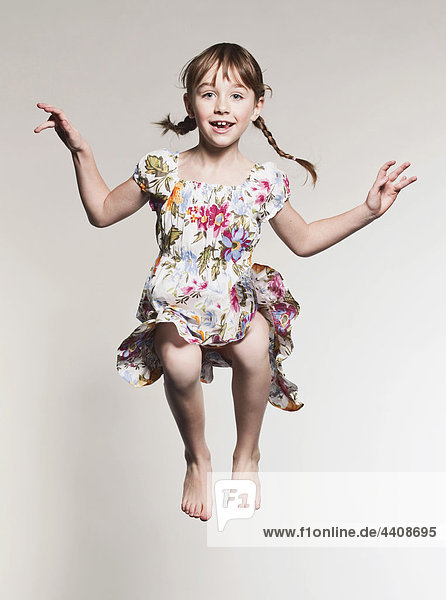 Girl (6-7) jumping against gray background  portrait  smiling