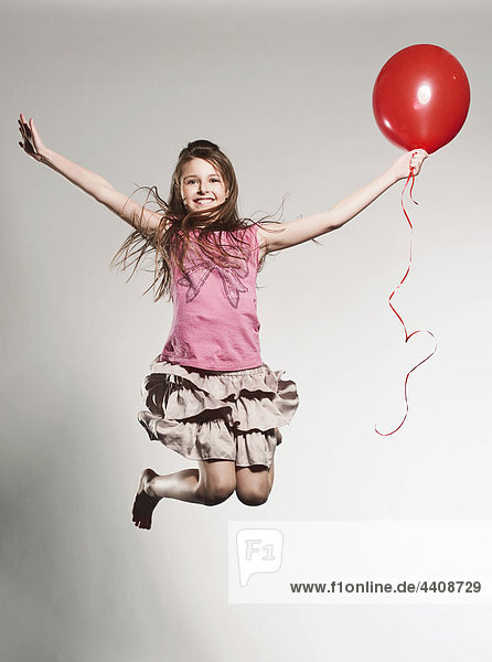 Girl (8-9) jumping with holding balloon  smiling  portrait
