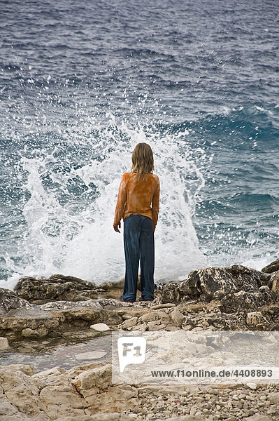 Croatia  Korcula  Girl (8-9) standing by sea looking at splashing wave  rear view