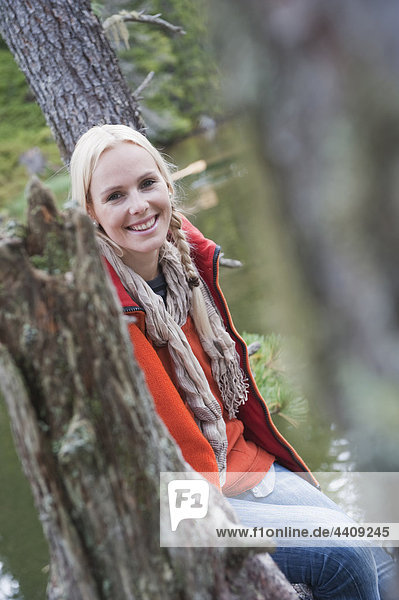 Österreich  Obertauern  Frau auf Baumstamm sitzend  lächelnd  Portrait
