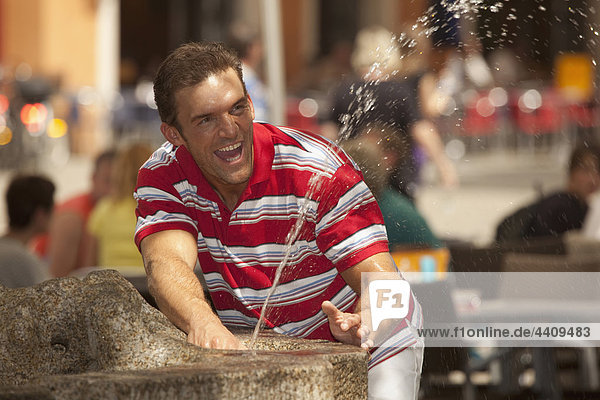 Man playing with fountain water  background people