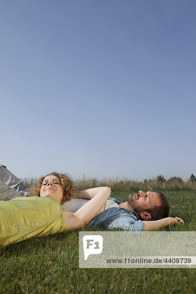 Mann und Frau liegen auf Gras und lächeln
