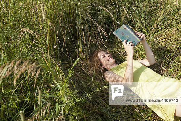 Frau auf Gras liegend und Buch lesend