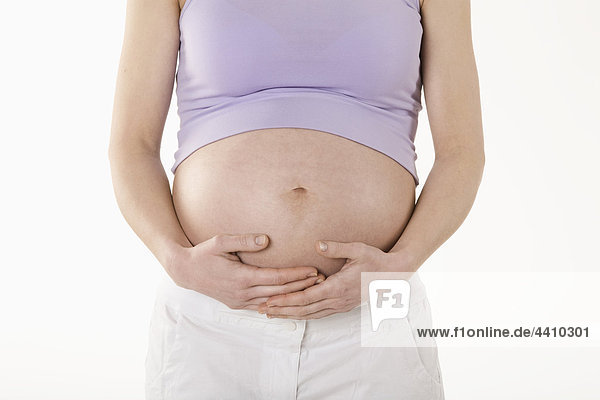 Schwangere Frau stehend mit Händen auf dem Bauch  Mittelteil