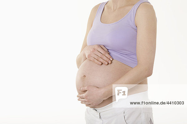 Schwangere Frau stehend mit Händen auf dem Bauch  Mittelteil