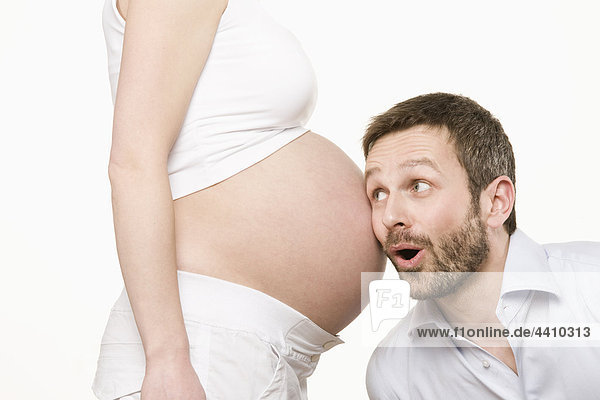 Man listening to pregnant woman's belly  smiling