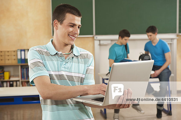 Young man using laptop with students in background