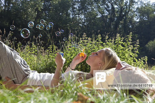 Young woman blowing bubble with lying on man
