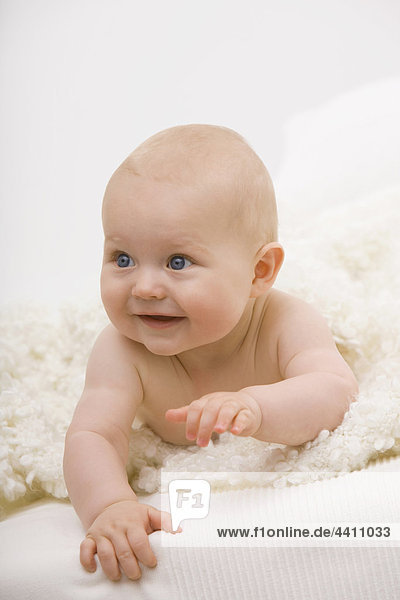 Baby boy (6-11 months) lying on bed  smiling  looking away