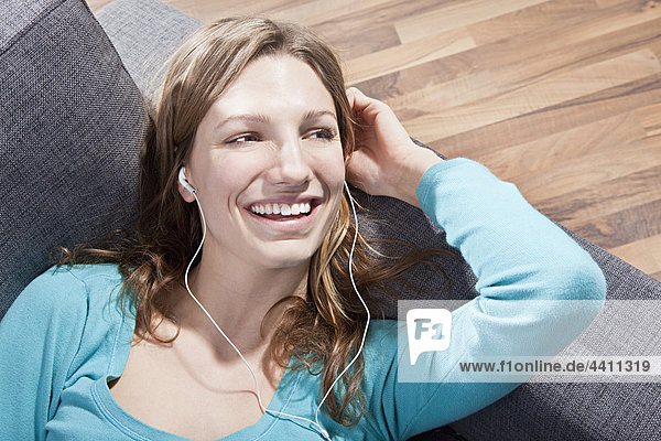 Frau entspannt sich auf der Couch und hört Musik  lächelt