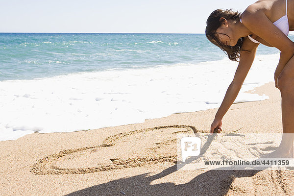 Frankreich  Korsika  Frau zeichnet Herzform in Sand am Strand