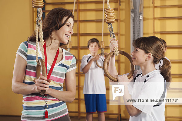 Woman and girl holding gymnastic rings with boy in background