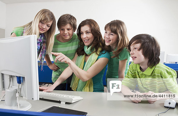 Germany  Emmering  Teacher using computer and explaining students  smiling