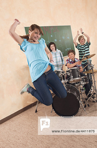 Girl jumping with boys in background playing drums
