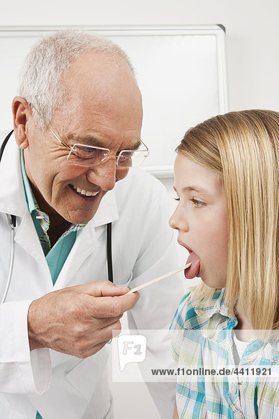 Arzt untersuchendes Mädchen (8-9) mit Zungenspatel