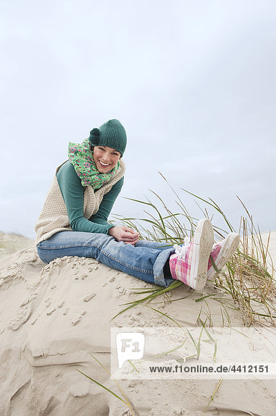 Deutschland  St. Peter-Ording  Nordsee  Frau auf Sanddünen sitzend  lächelnd