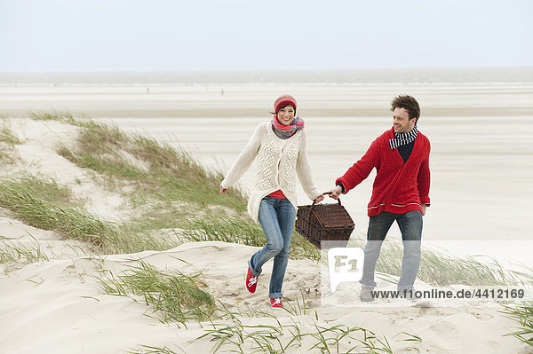 Germany  St.Peter-Ording  North Sea  Couple holding picnic basket walking on beach
