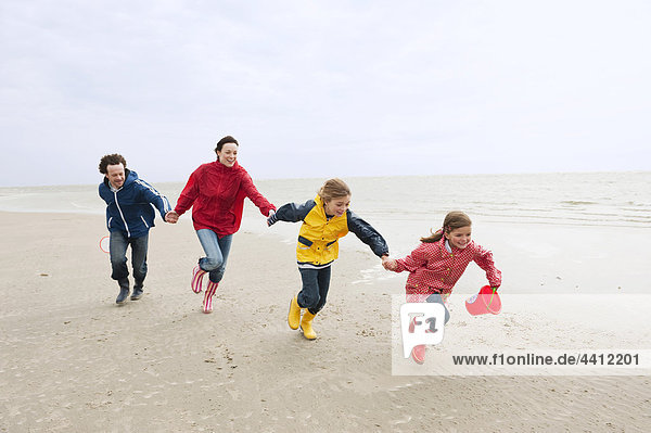 Germany  St. Peter-Ording  North Sea  Family holding hands and running on beach