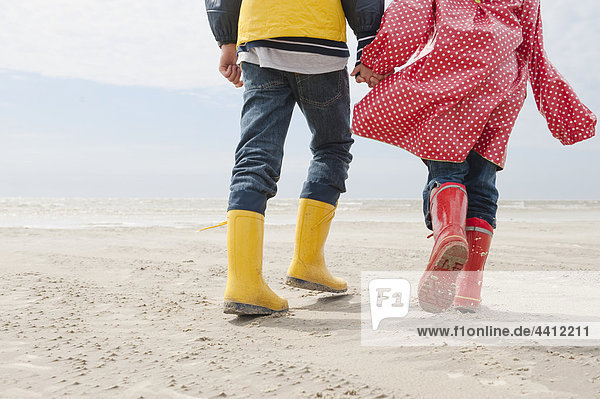 Germany  North Sea  St.Peter-Ording  Children (6-9) wearing boots and rain coats walking on beach  low section
