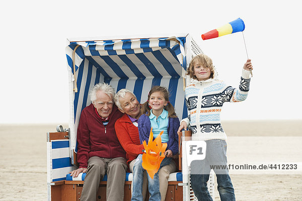 Deutschland  St. Peter-Ording  Nordsee  Großeltern mit Kindern (6-9) auf Kapuzenstrandstuhl sitzend