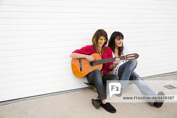 Zwei Mädchen auf dem Boden sitzend mit Gitarre