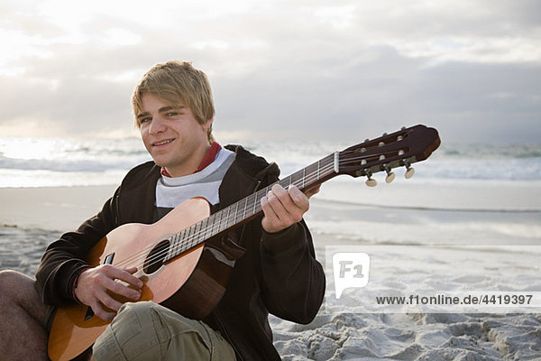 Junger Mann spielt Gitarre am Strand