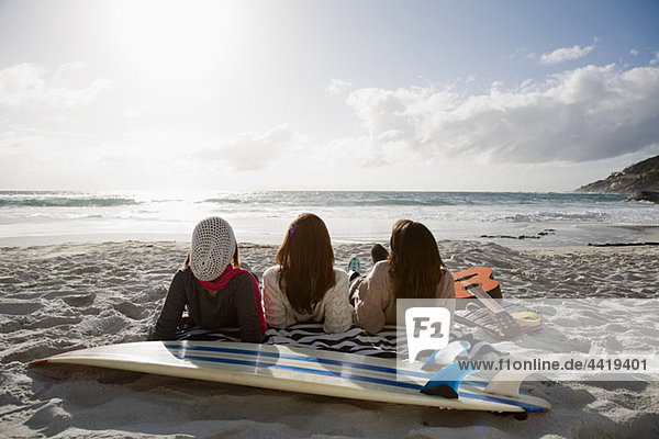 Drei Mädchen am Strand liegend mit Surfbrett