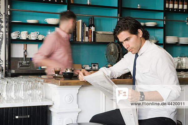 Man with newspaper and waiter in cafe