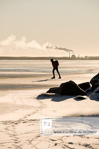 Silhouette der Mann Eislaufen auf gefrorenen See  Fabrik im Hintergrund