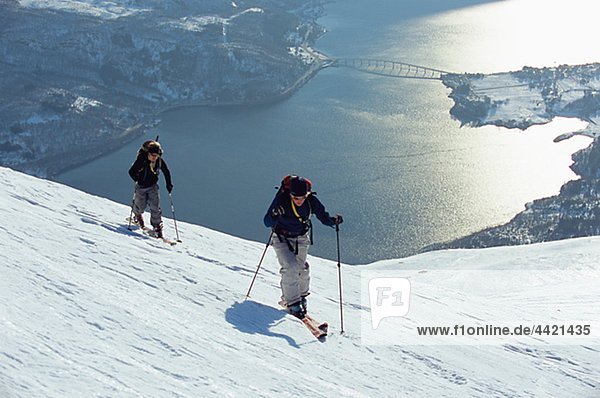 Two people telemark skiing in winter scenery  Lake Mjosa in background