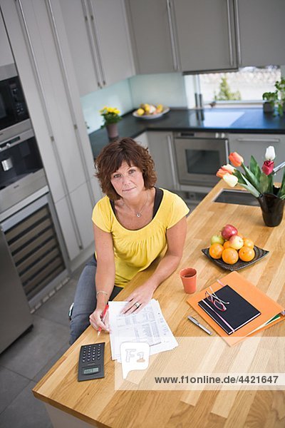 Frau sitzt in Küche mit Rechnungen  Portrait