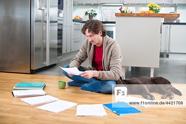 Mid-adult man doing paperwork on floor  while dog is sleeping next to him