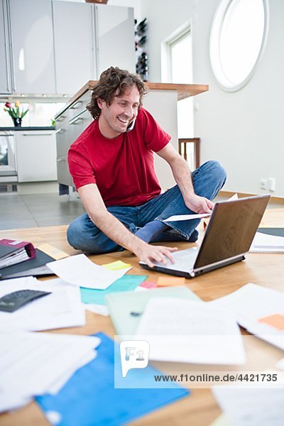 Cheerful man doing domestic paperwork on floor