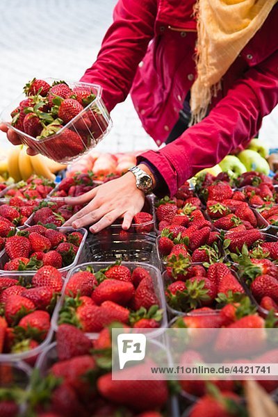Close-up mid section of woman choosing strawberries at fruit market